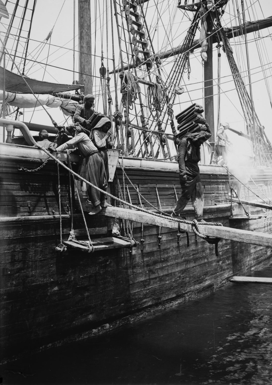 Porters carrying goods down a plank from a sailing vessel in the harbour of Beirut, photographed around 1900