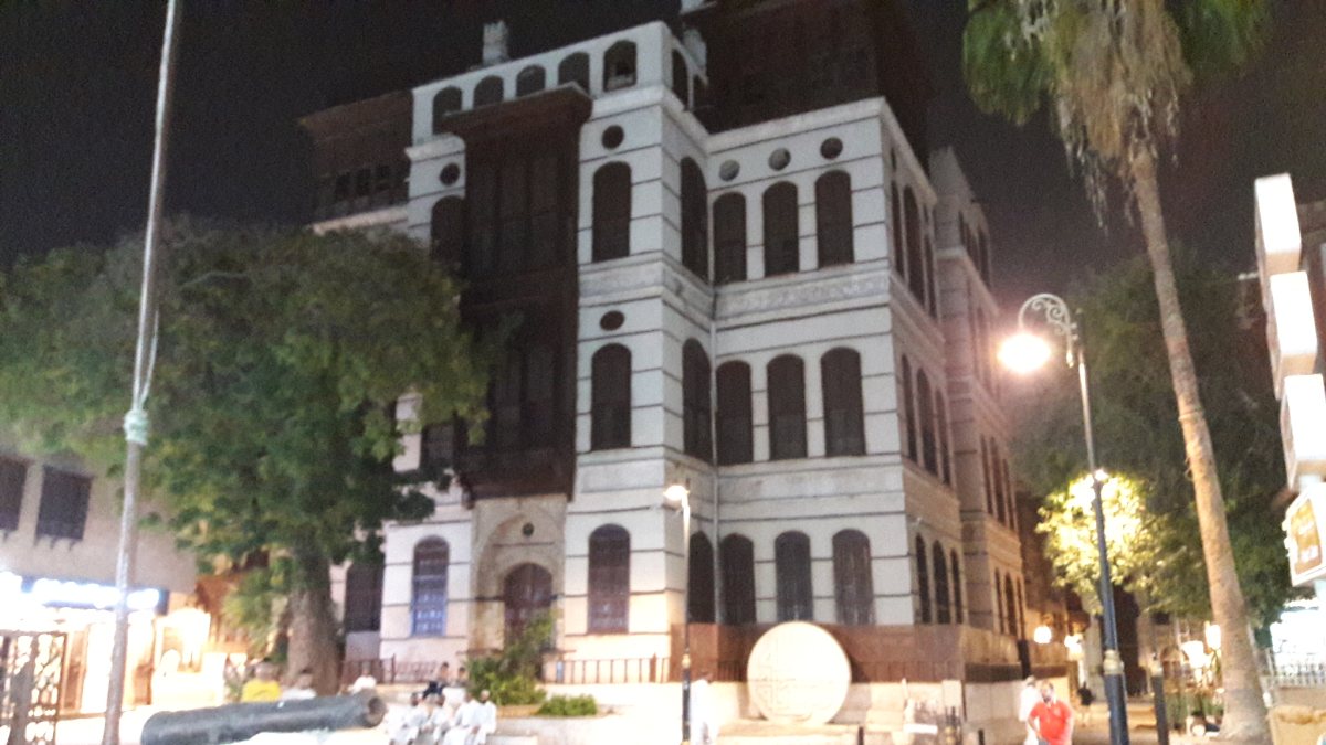 Bayt Nasseef at night in its Al-Balad streetscape, framed by trees and lamps